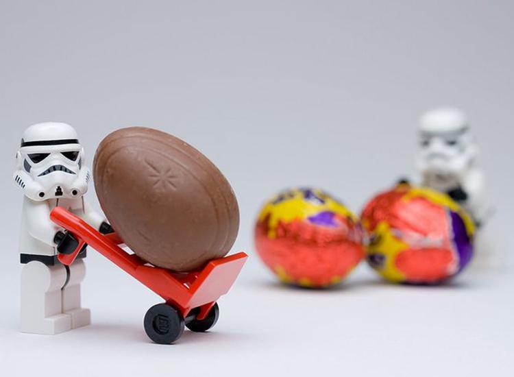 A LEGO Stormtrooper pushing around Cadbury eggs against a white background.