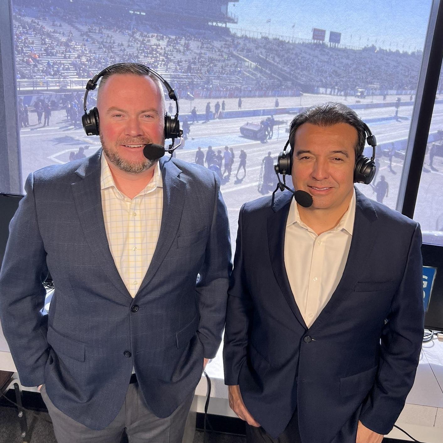 NHRA play-by-play broadcasters Brian Lohnes and Tony Pedregon standing in front of a window overlooking the In-N-Out Burger drag strip in Ponoma, California in November 2022.