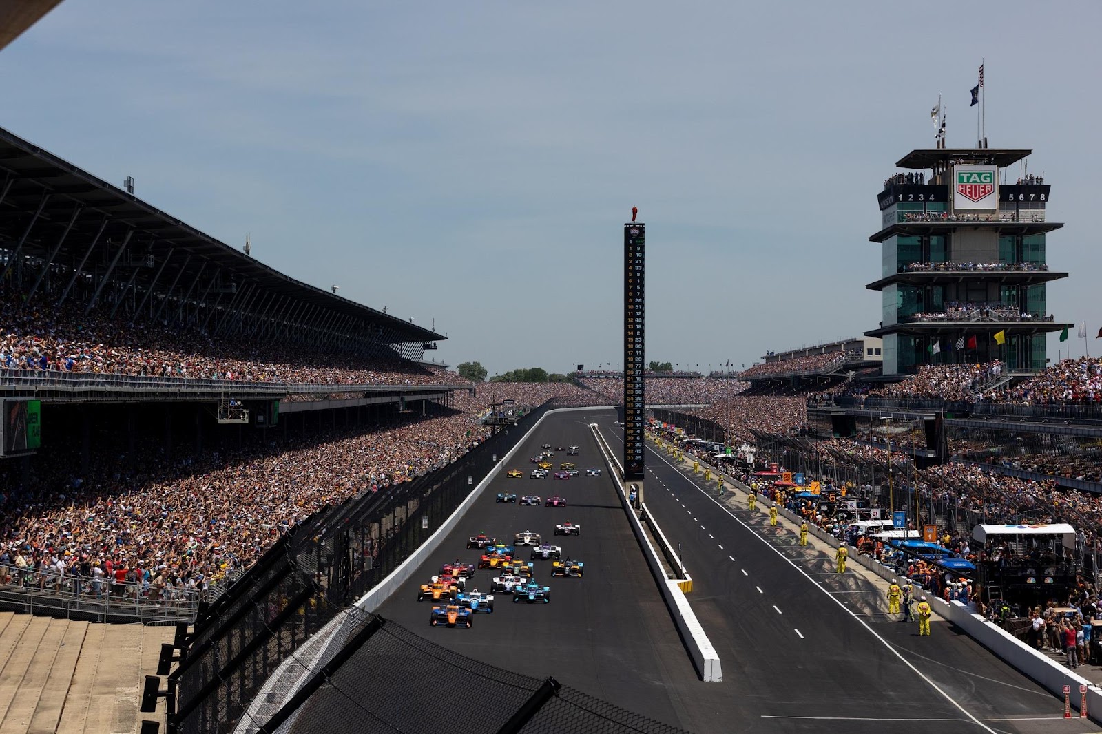 The start of the 2022 Indianapolis 500 with IndyCar racecars streaking down the frontstretch into Turn 1.